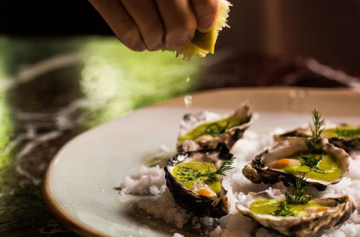 A person squeezing lime onto oysters.